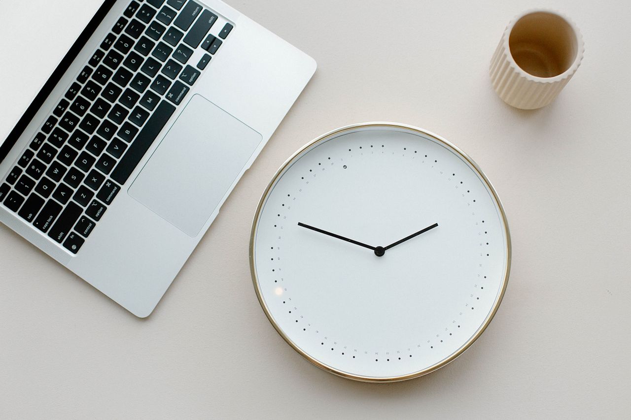 Analoge Uhr neben einem Laptop